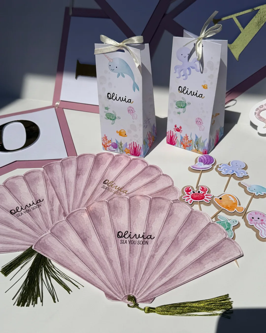 Abanicos de papel rosa con nombre, cajitas y figuras marinas
