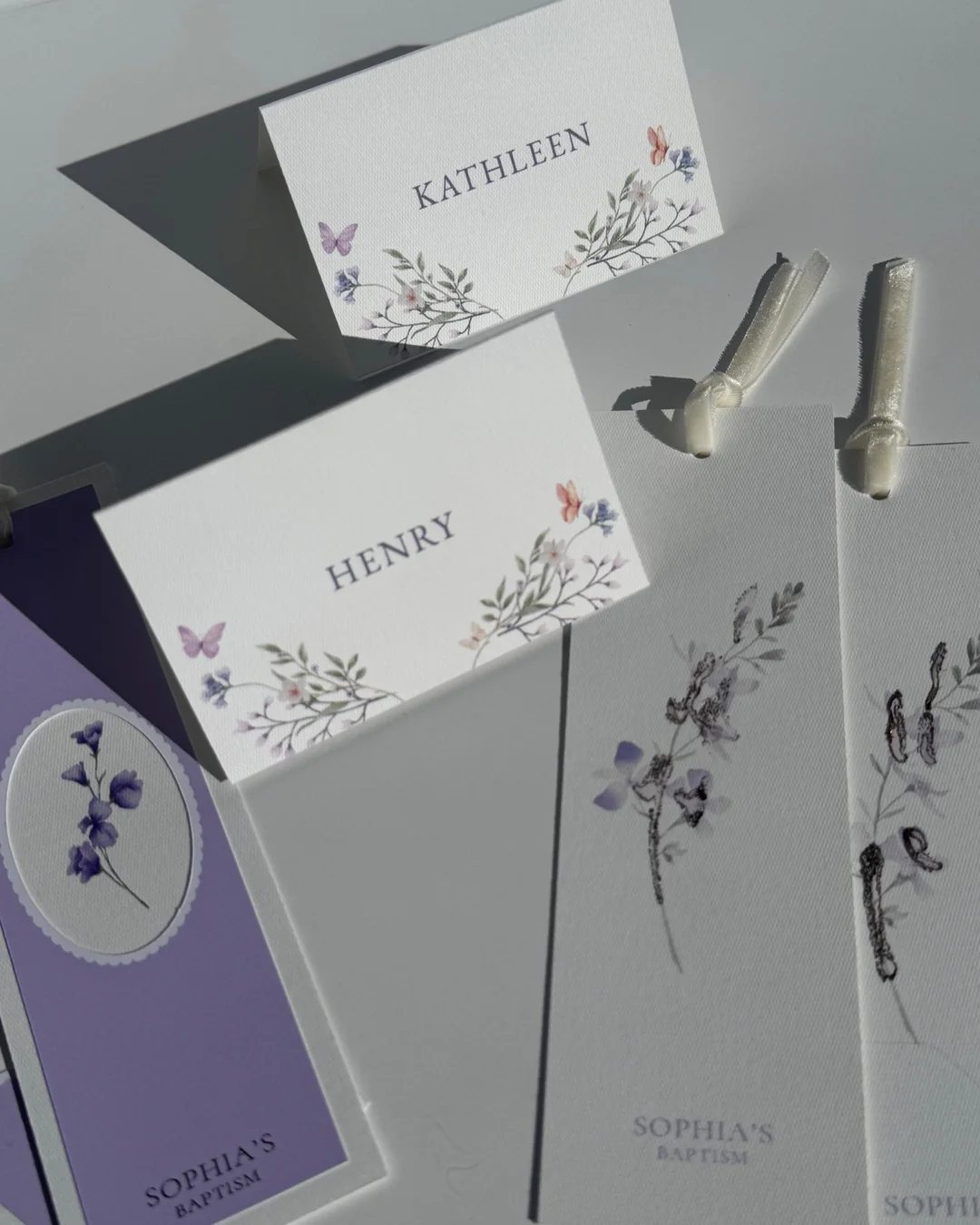 Tarjetas de lugar con flores y mariposas, y piezas lilas de un bautizo